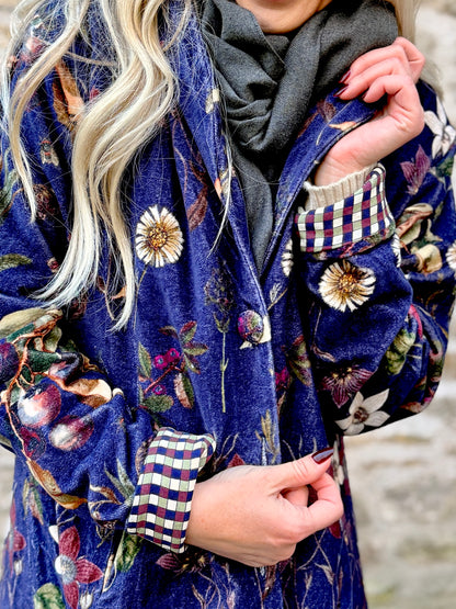 Wrap yourself in autumn warmth with this long velvet coat in a rich Rosehip Design Winter Floral that perfectly echoes the season. The beautiful plum tones on navy blue are perfect for this time of year. The soft velvet exterior is complemented by a classic check lining, adding a touch of style to its bold, modern silhouette. Luxuriously warm yet effortlessly wearable, it’s the perfect layer for crisp autumn days — whether you’re strolling through the countryside or heading into the city.