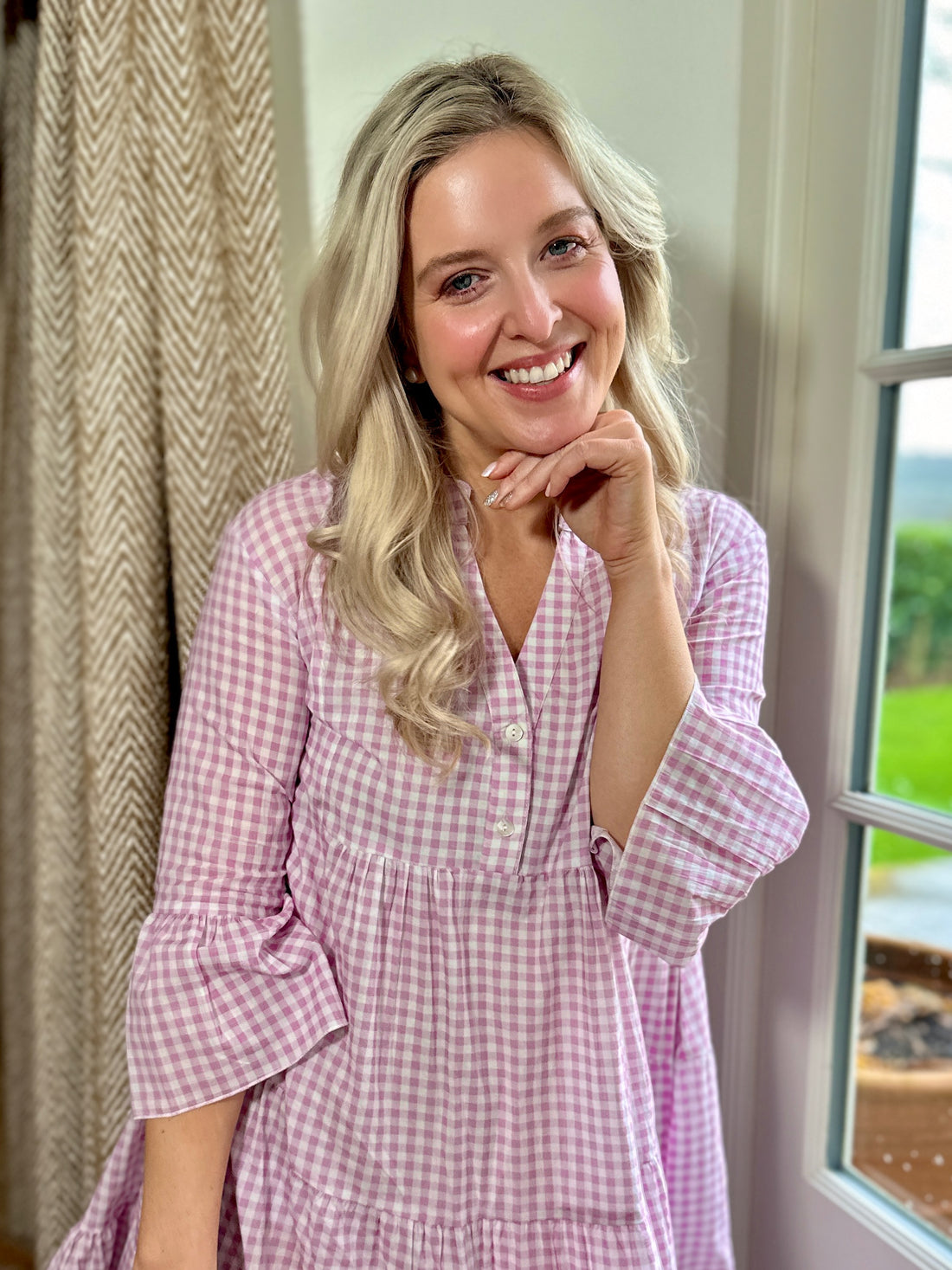 Rosehip Design Chloe Dress in Gingham Primrose is a classic summer floral tiered dress in a warm pink checked Gingham print with lovely long angel sleeves and side pockets, made from 100% soft Indian Cotton, packed in a matching bag.