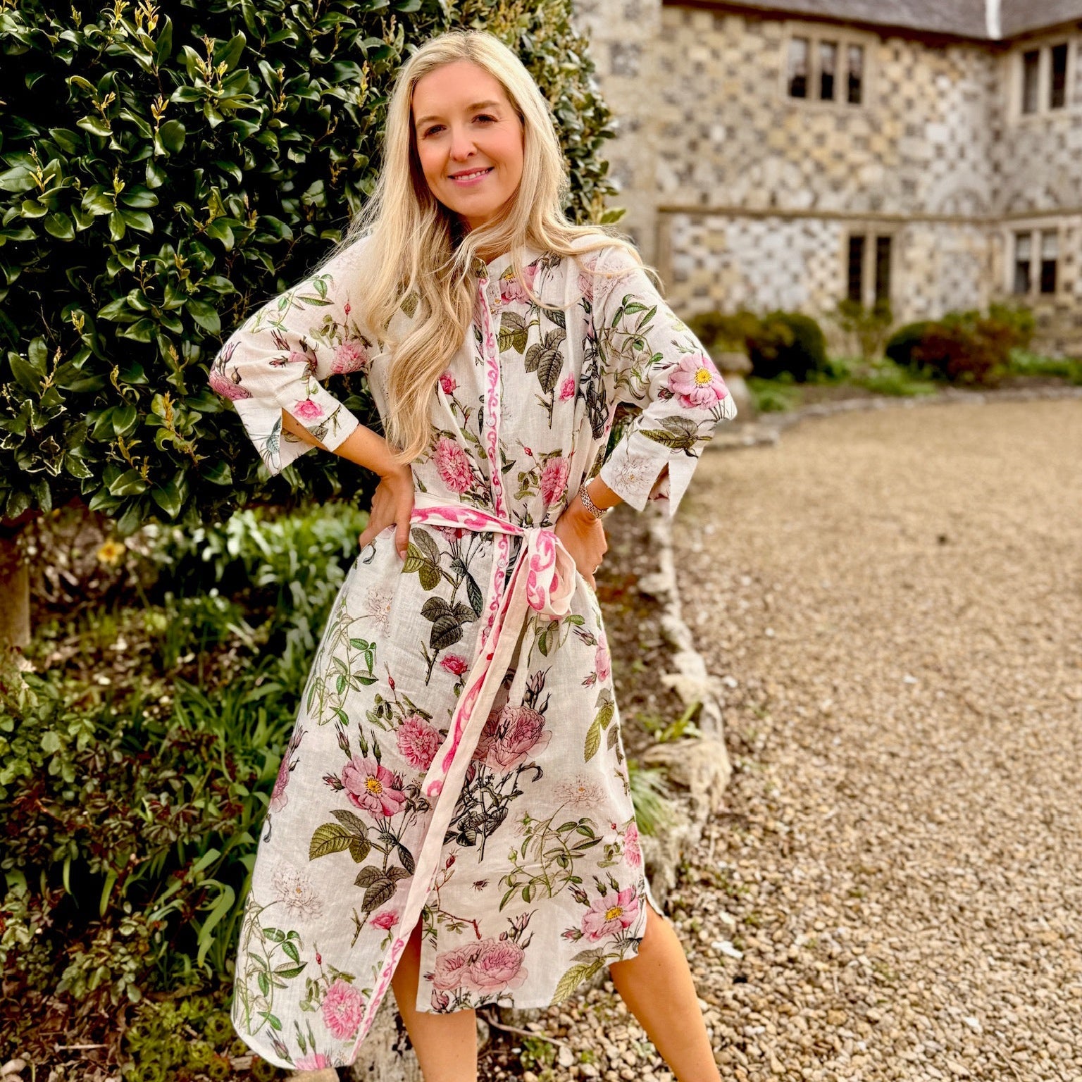 Woman in a Rosehip floral dress standing outdoors near a stone building.